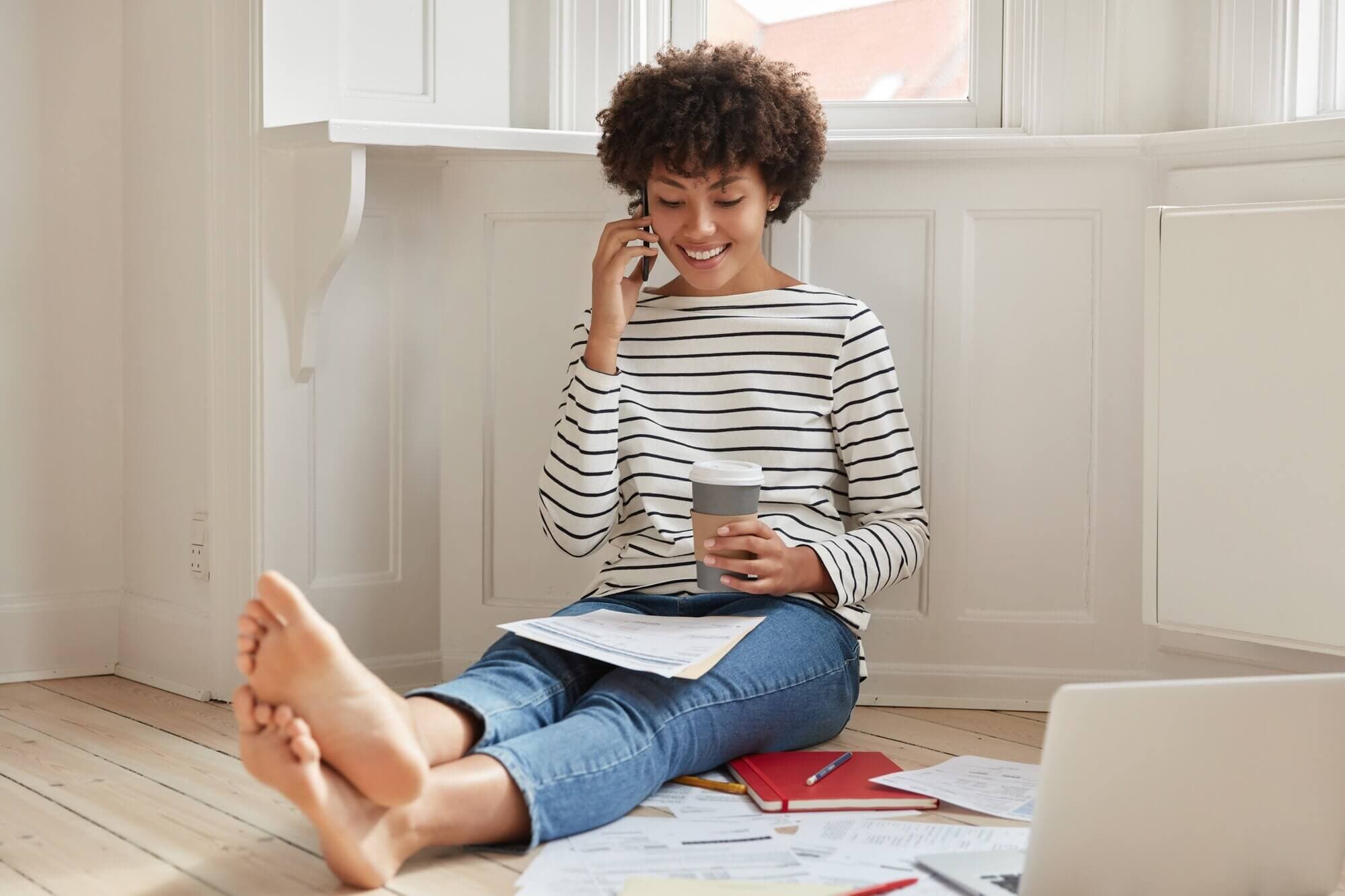 A woman reviews paperwork while speaking on her phone from home.