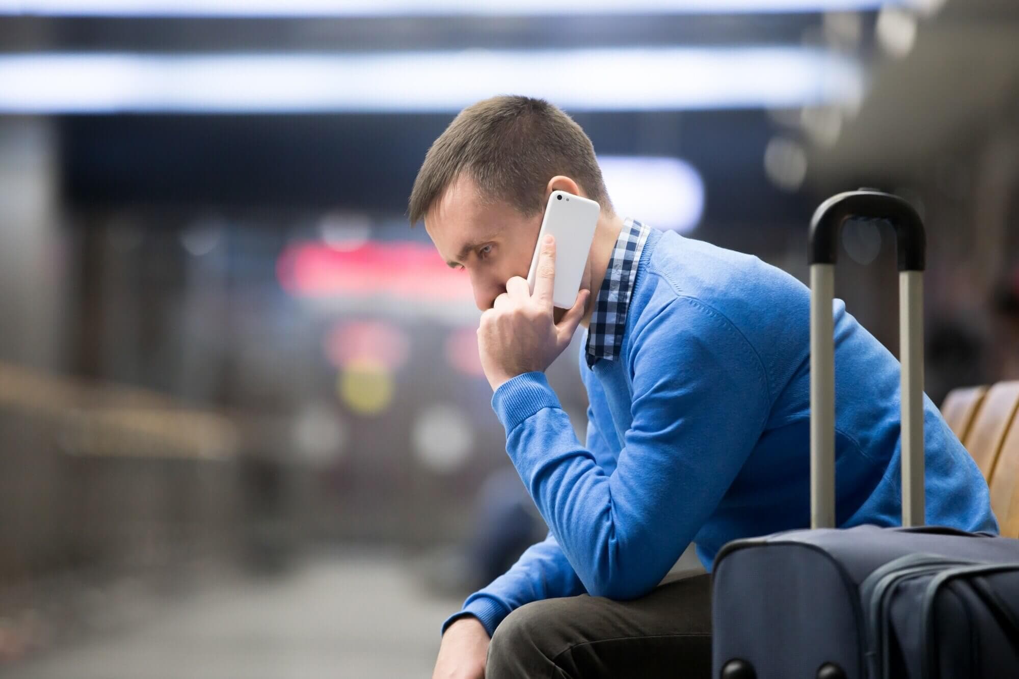 A traveler takes a phone call while waiting with luggage in an airport terminal.