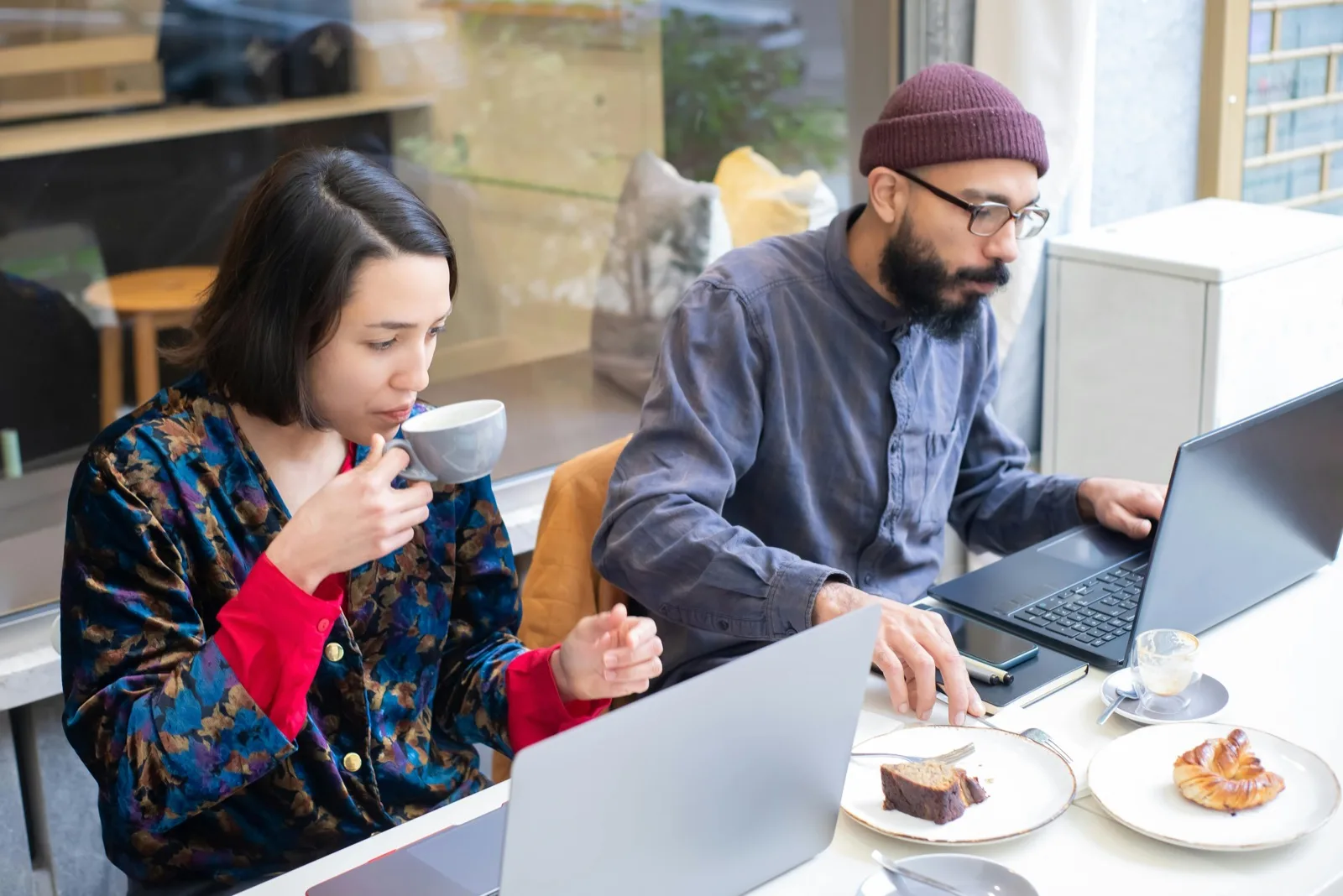 Two people working on laptops over coffee in a cafe abroad