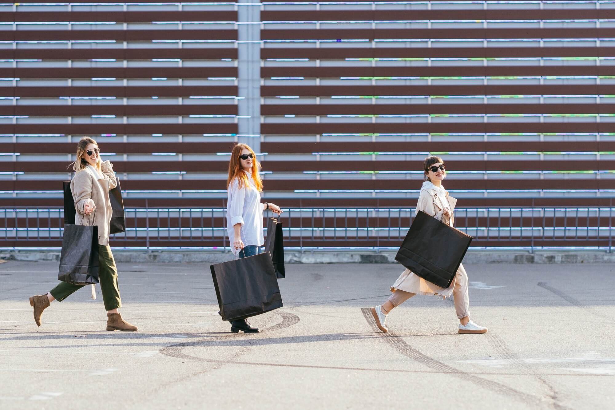 Two women walk through a city street carrying shopping bags and chatting.
