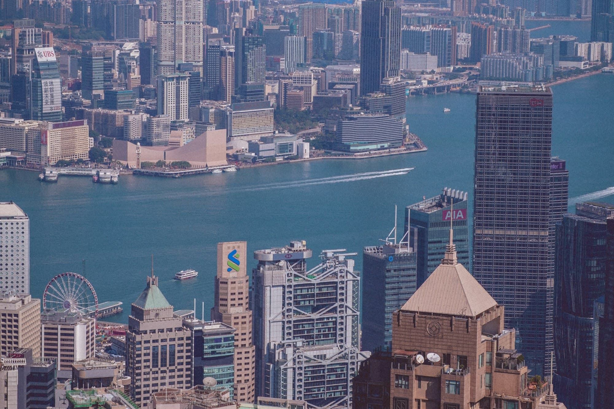 A wide harbor skyline shows ferries, towers, and dense waterfront development.