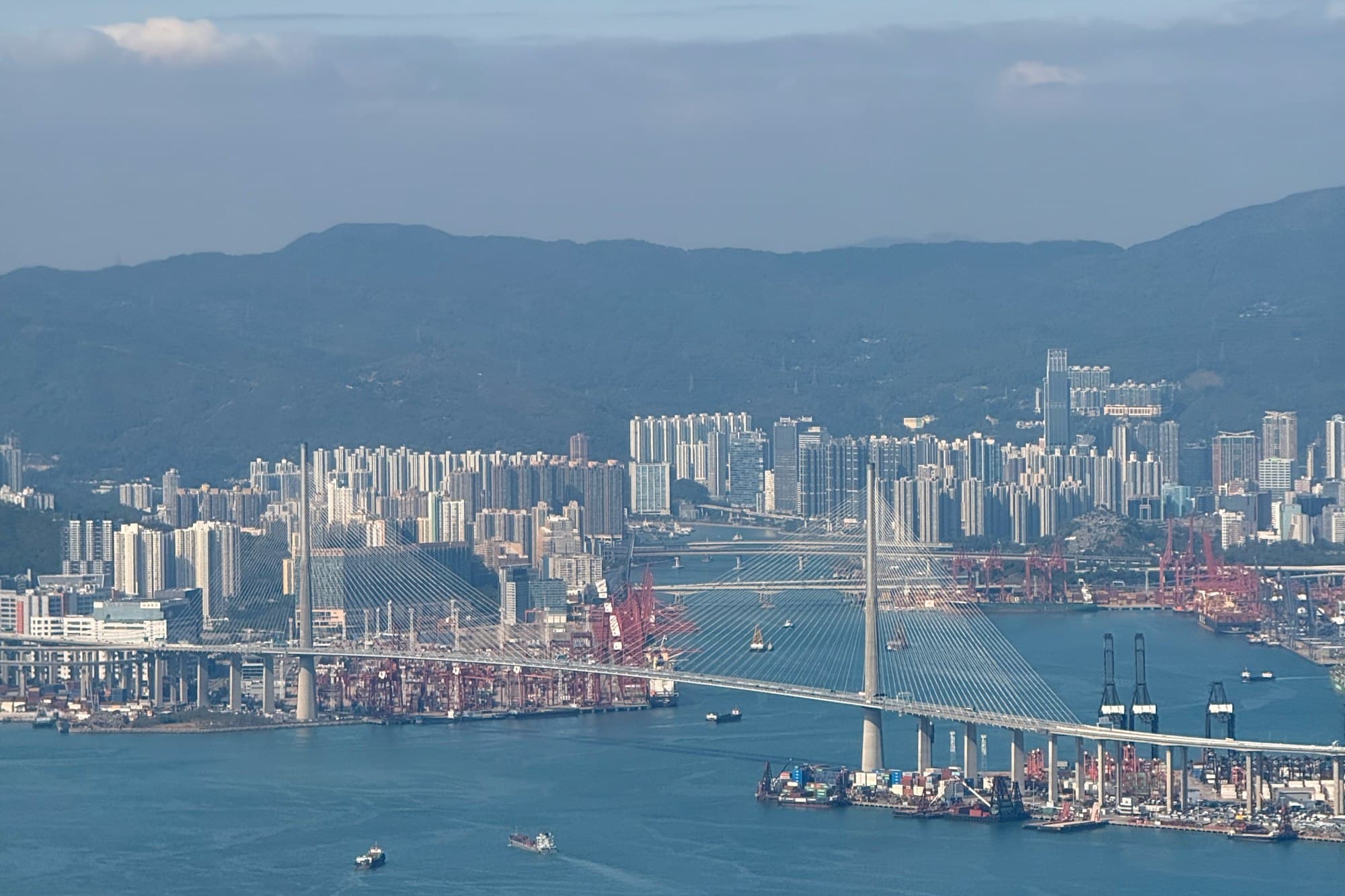 Ships and cranes fill a busy harbor in front of a city skyline.