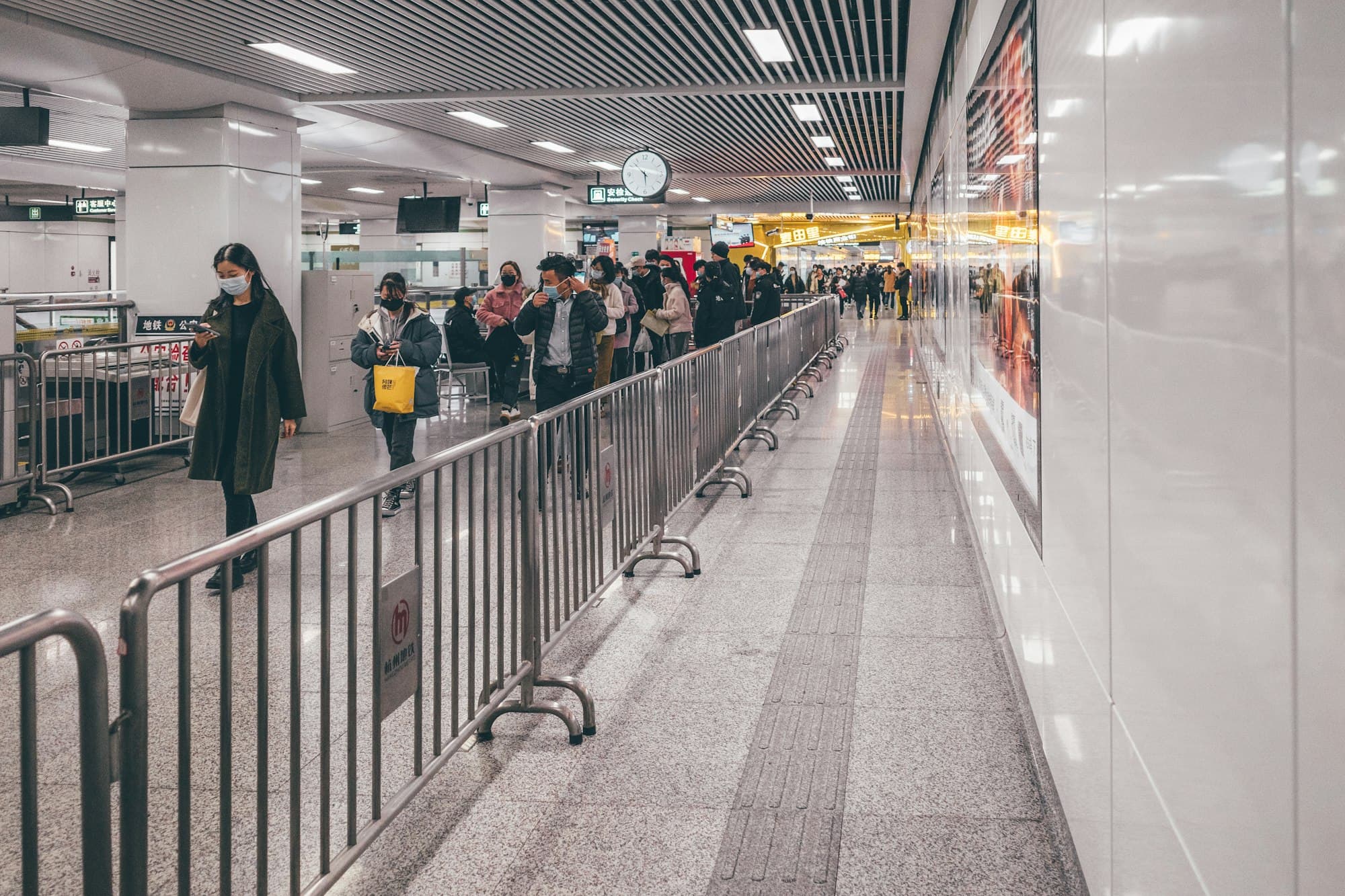 Travelers wait in a long line inside a crowded airport hall.