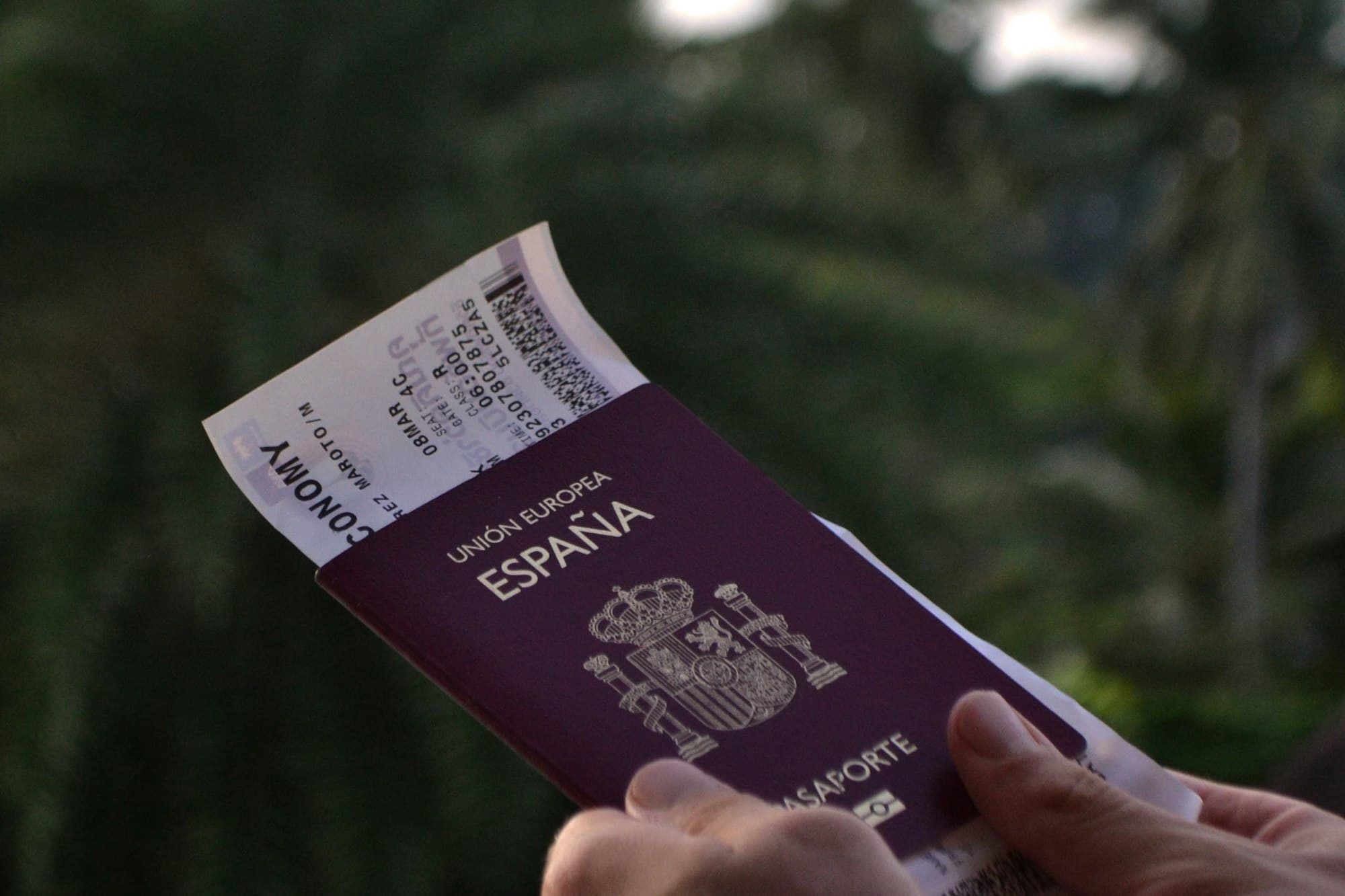 A traveler holds a passport and boarding pass against a dark green background.