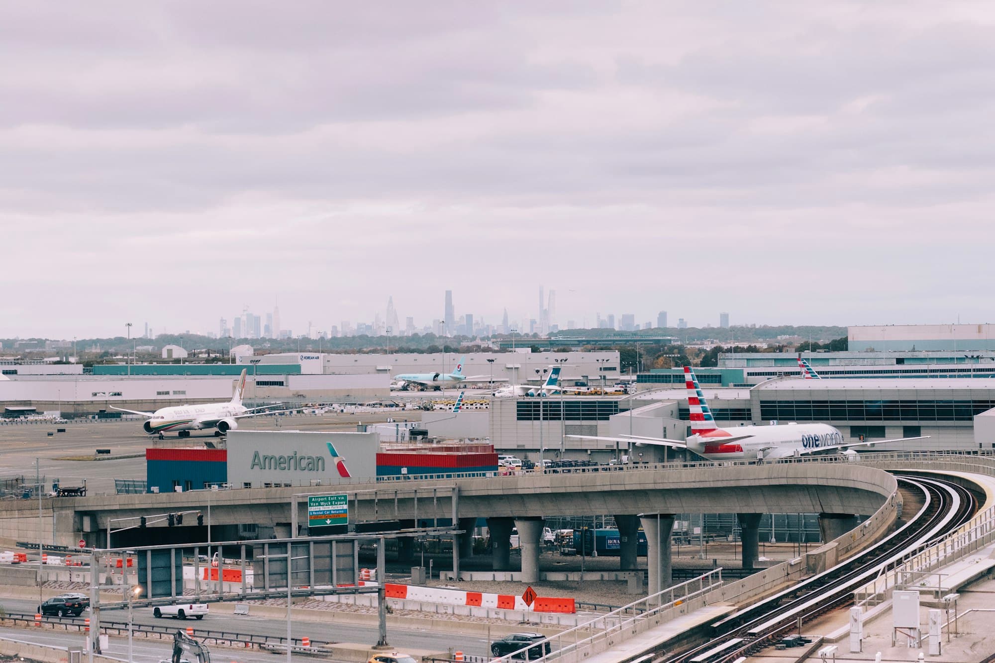 Airliners stand on a runway with a city skyline beyond the airport.