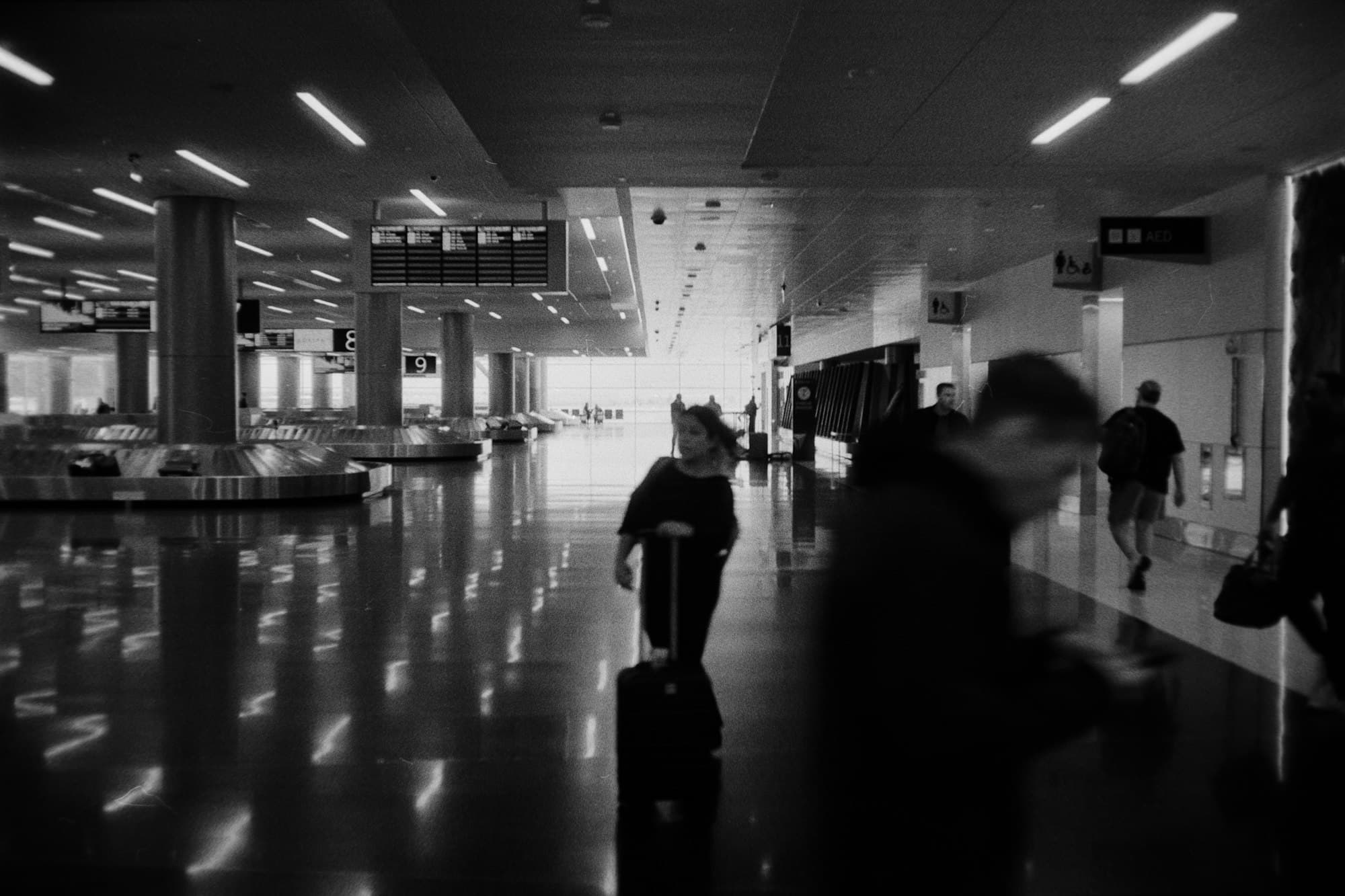 People walk through a clean modern airport terminal beneath directional signage.