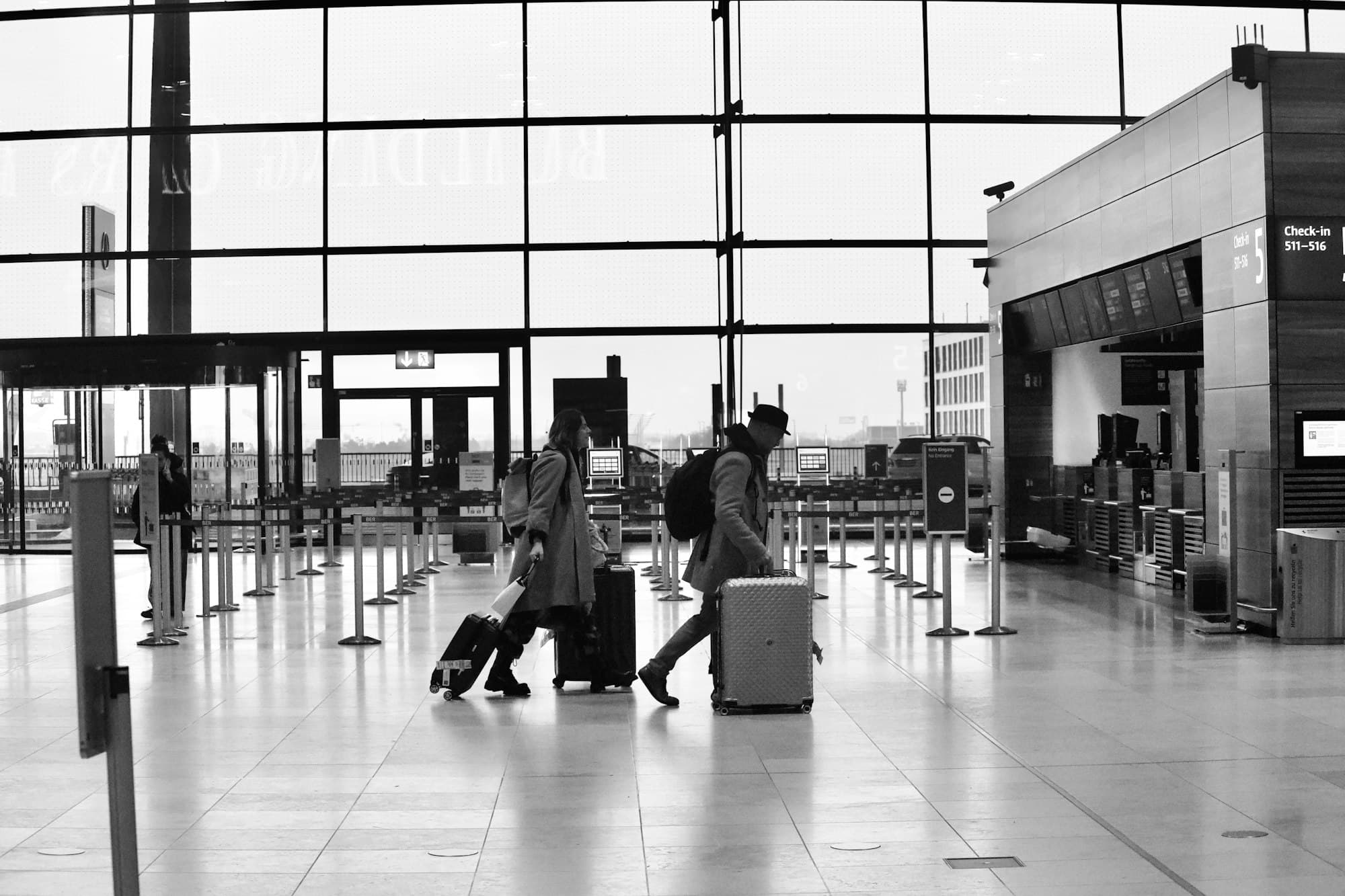 Travelers with rolling luggage walk through an airport terminal.