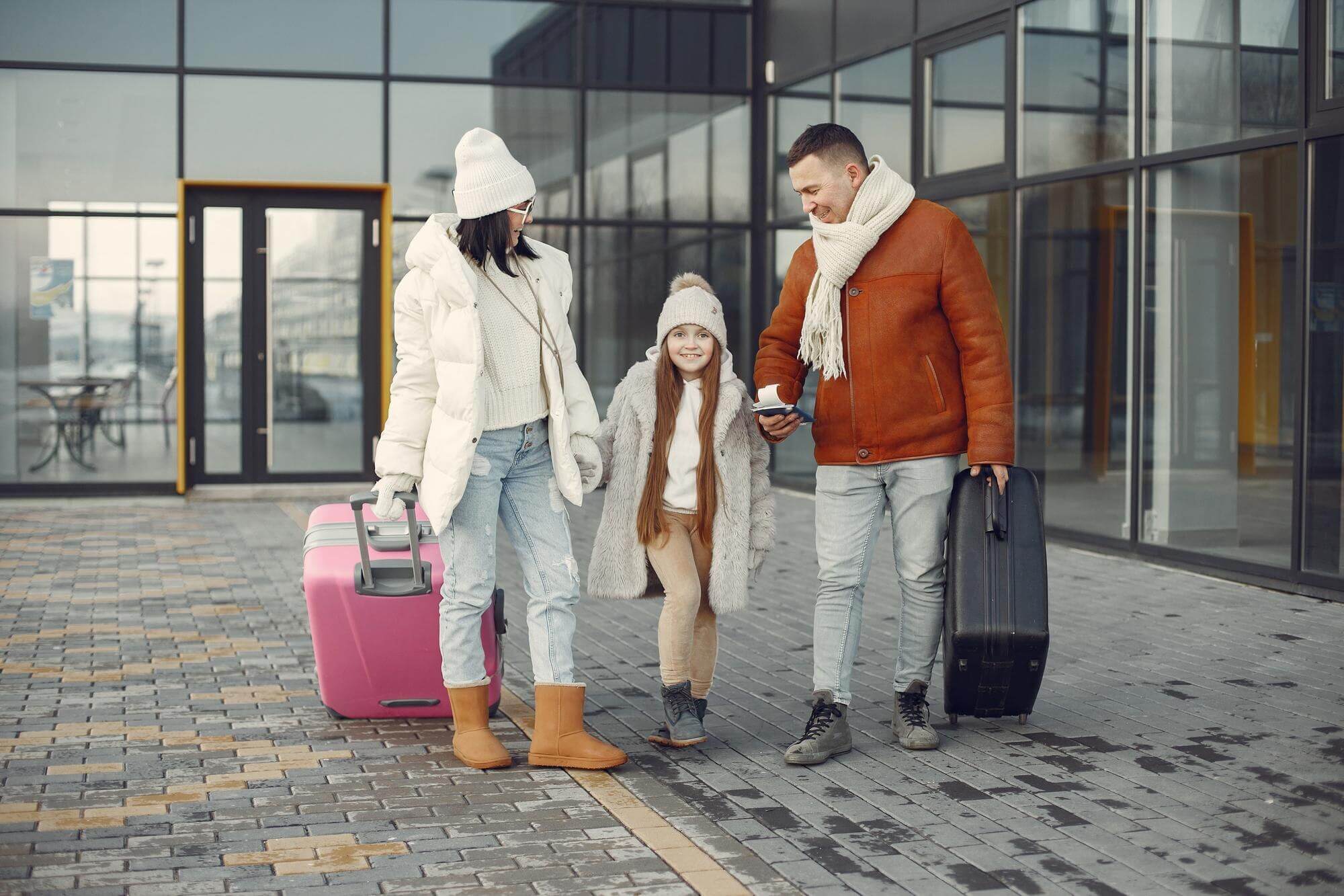 A family walks through an airport terminal with luggage and a child in tow.
